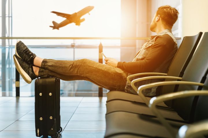 Travel Safe - man sitting on gang chair with feet on luggage looking at airplane