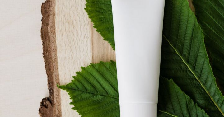 Beauty Essentials - Top view of chestnut green leaf and mockup of skin care or hair care cosmetic product placed on wooden surface