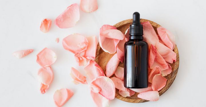 Beauty Essentials - Top view of empty brown bottle for skin care product placed on wooden plate with fresh pink rose petals on white background isolated